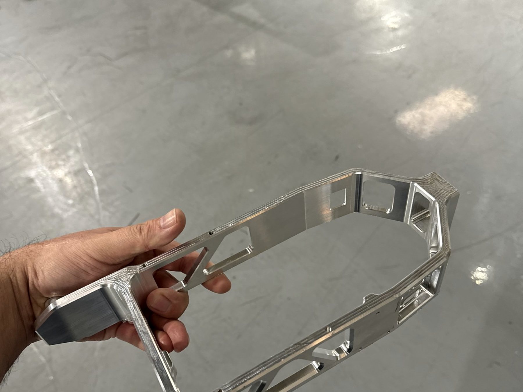 Machinist holding a finished aluminum bracket on the shop floor