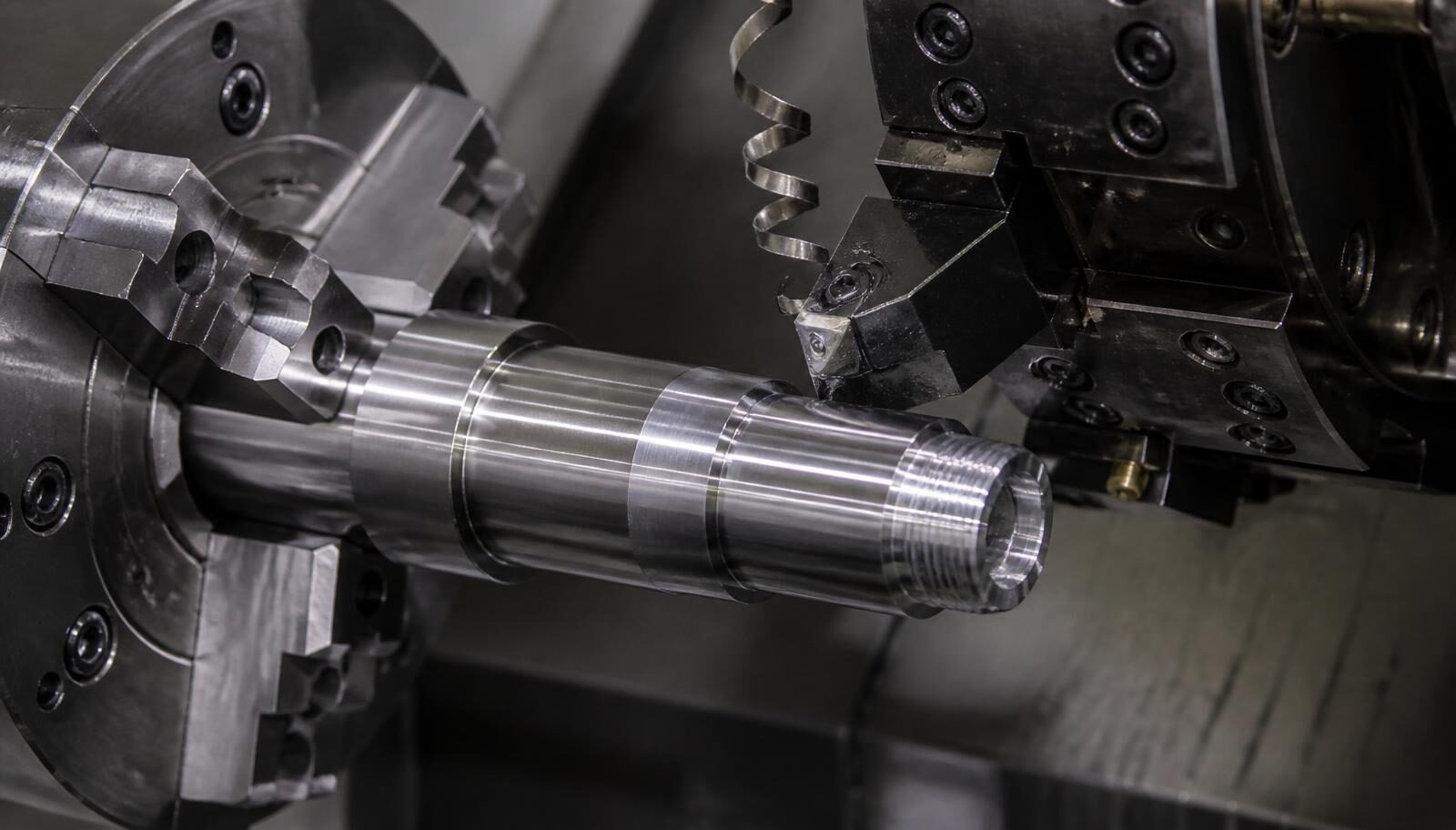 Close-up of a CNC turning center chuck holding a polished steel shaft mid-cut with a chip peeling from the insert